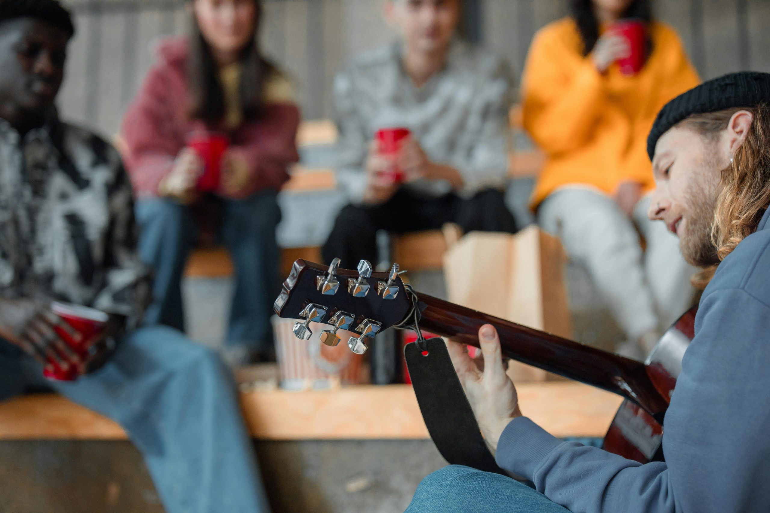 Casual gathering of friends enjoying acoustic guitar music at an outdoor venue.